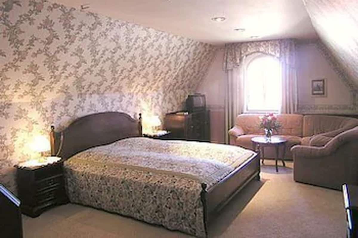 A bedroom with a bed, a chair, a small table, and a television.