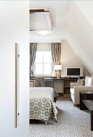 A compact hotel room with a bed, a desk with a computer, a television, and a seating area. - Burg-Hotel Relais du Silence (Rothenburg ob der Tauber)