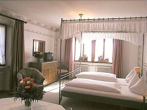 Une chambre avec deux lits, une commode, une chaise, un miroir et une fenêtre avec des rideaux.