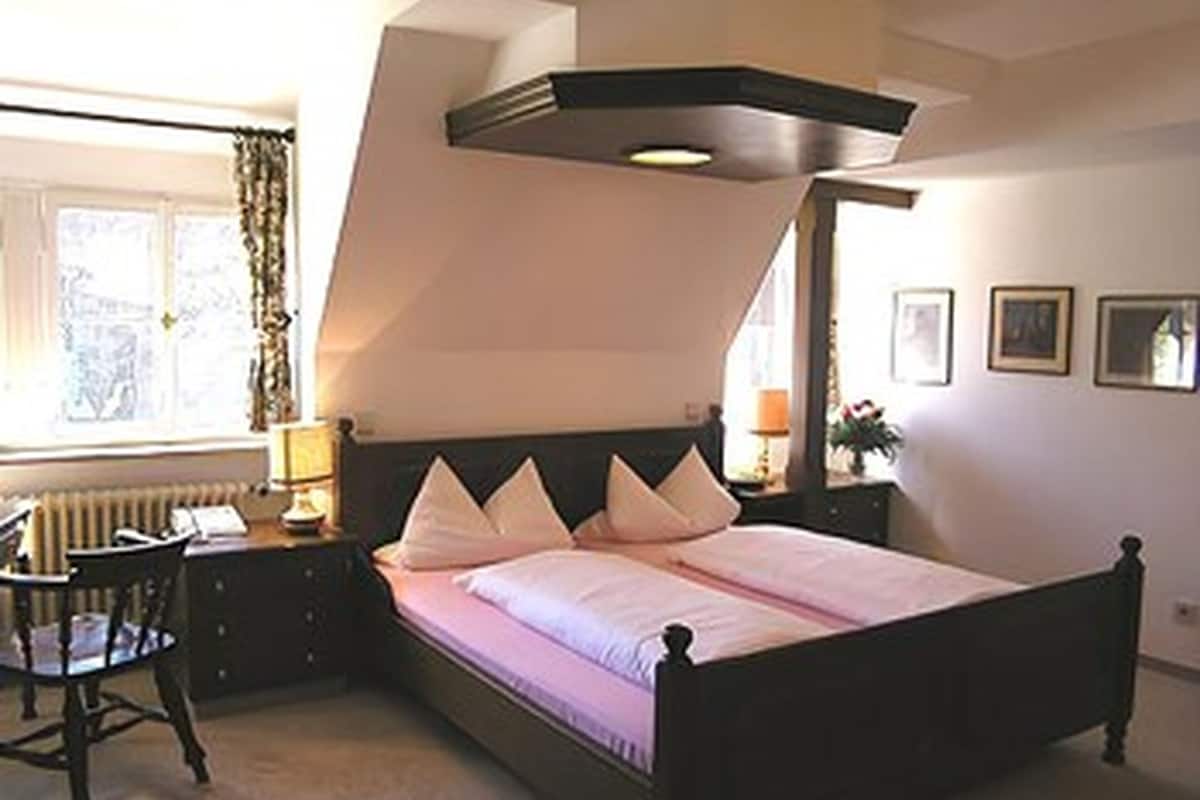 A bedroom with a bed, a chair, a nightstand, and a window with curtains.