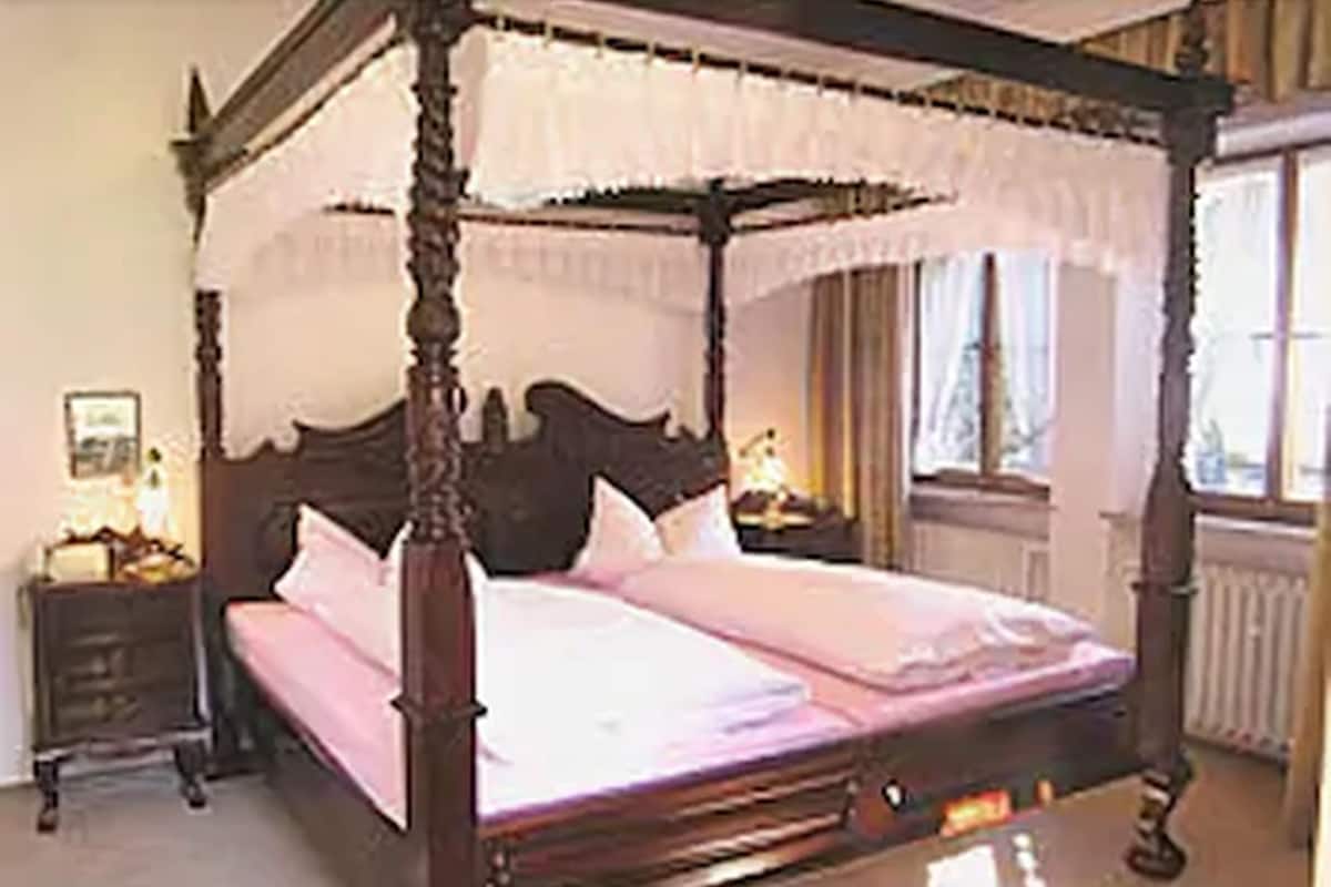 A four-poster bed with a canopy, a nightstand with a lamp, and a window with curtains.
