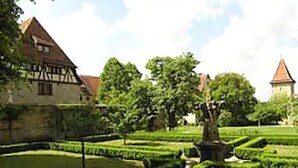 Un bâtiment historique à la façade traditionnelle en colombages, entouré de jardins bien entretenus et sous un ciel dégagé.