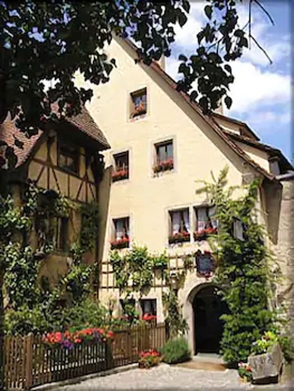A traditional European building with a sloped roof, multiple windows with flower boxes, and a wooden fence. - Burg-Hotel Relais du Silence (Rothenburg ob der Tauber)