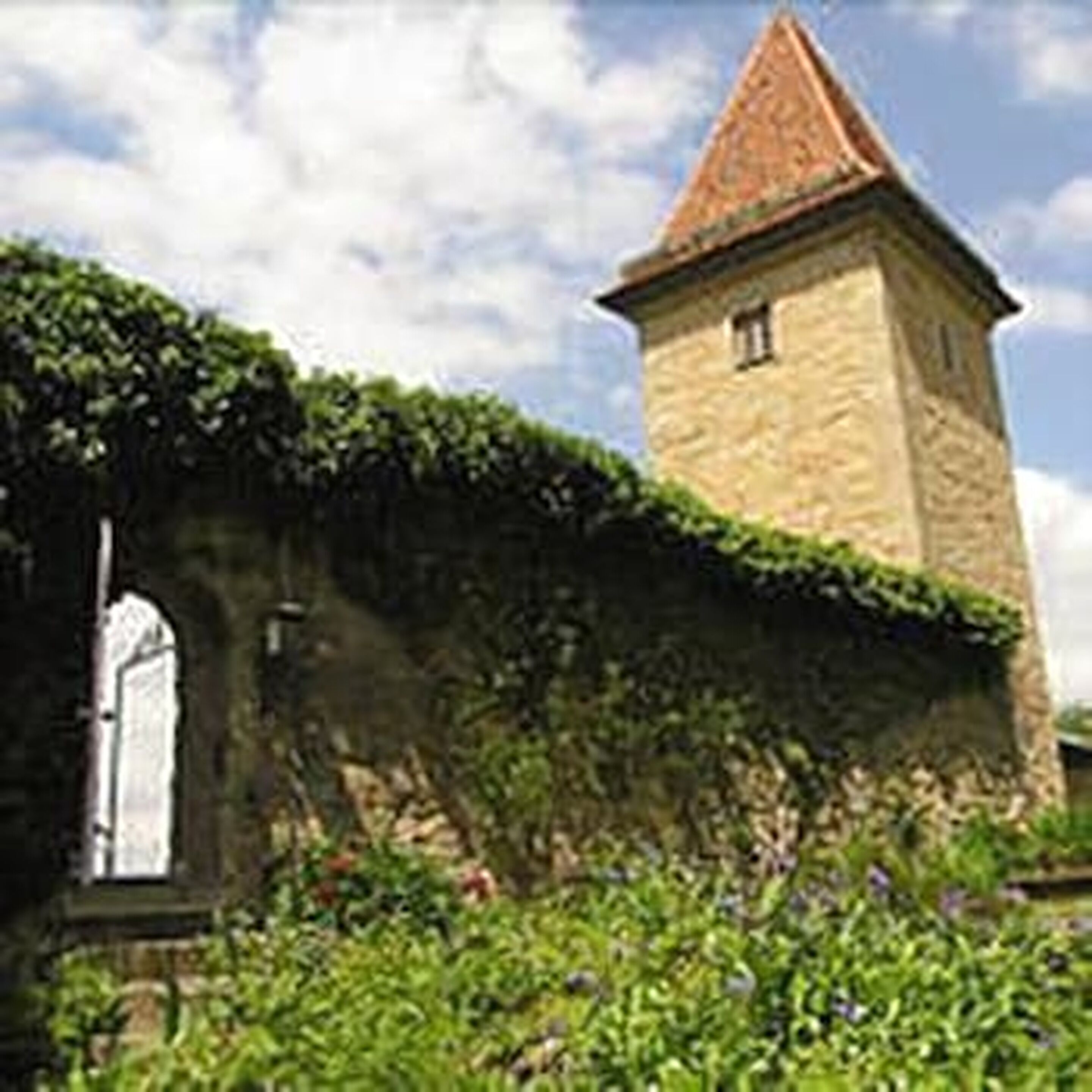 A stone tower with a conical roof, surrounded by greenery and a stone wall.