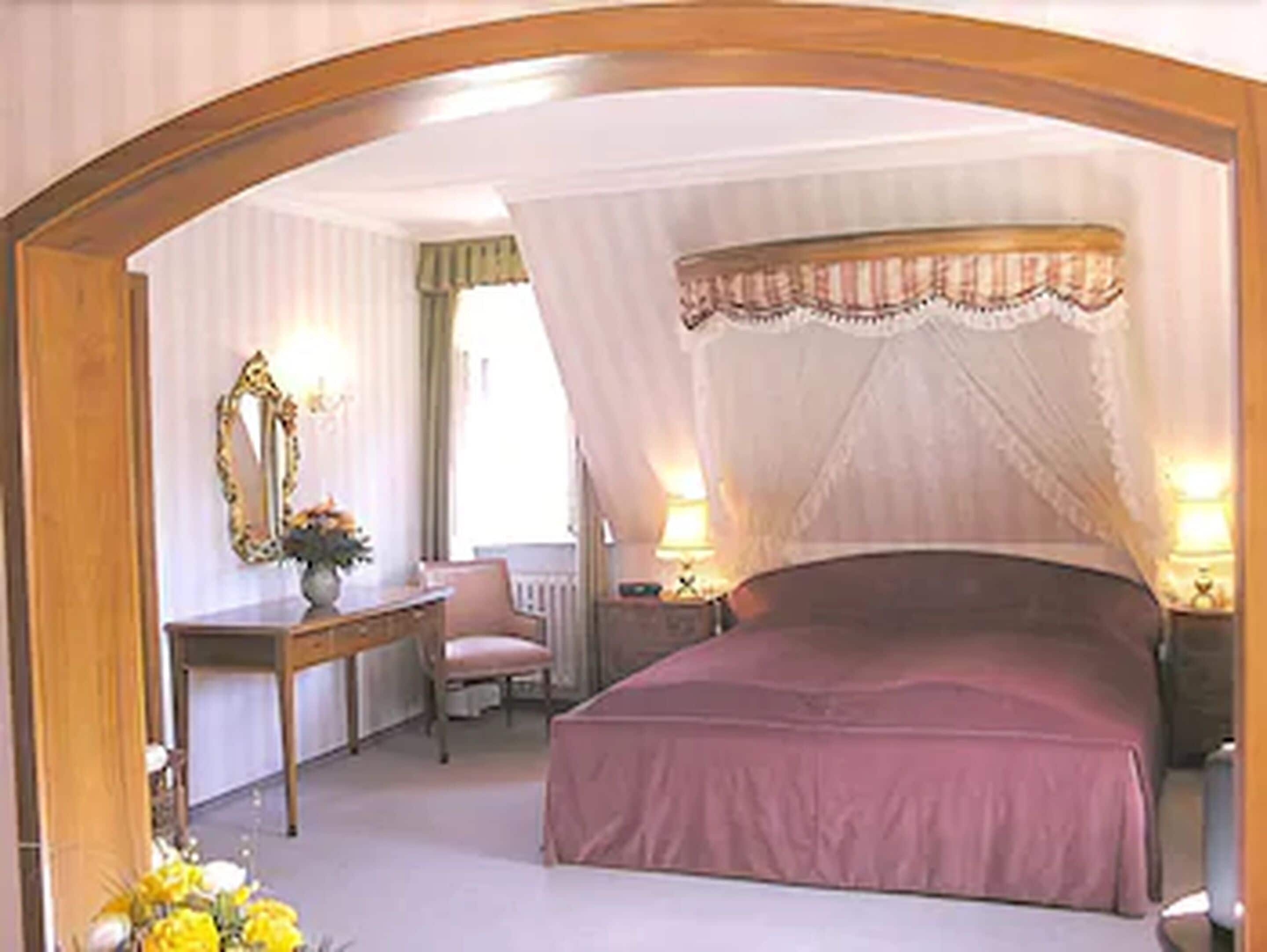 A bedroom with a canopy bed, a bedside table, a chair, and a mirror.