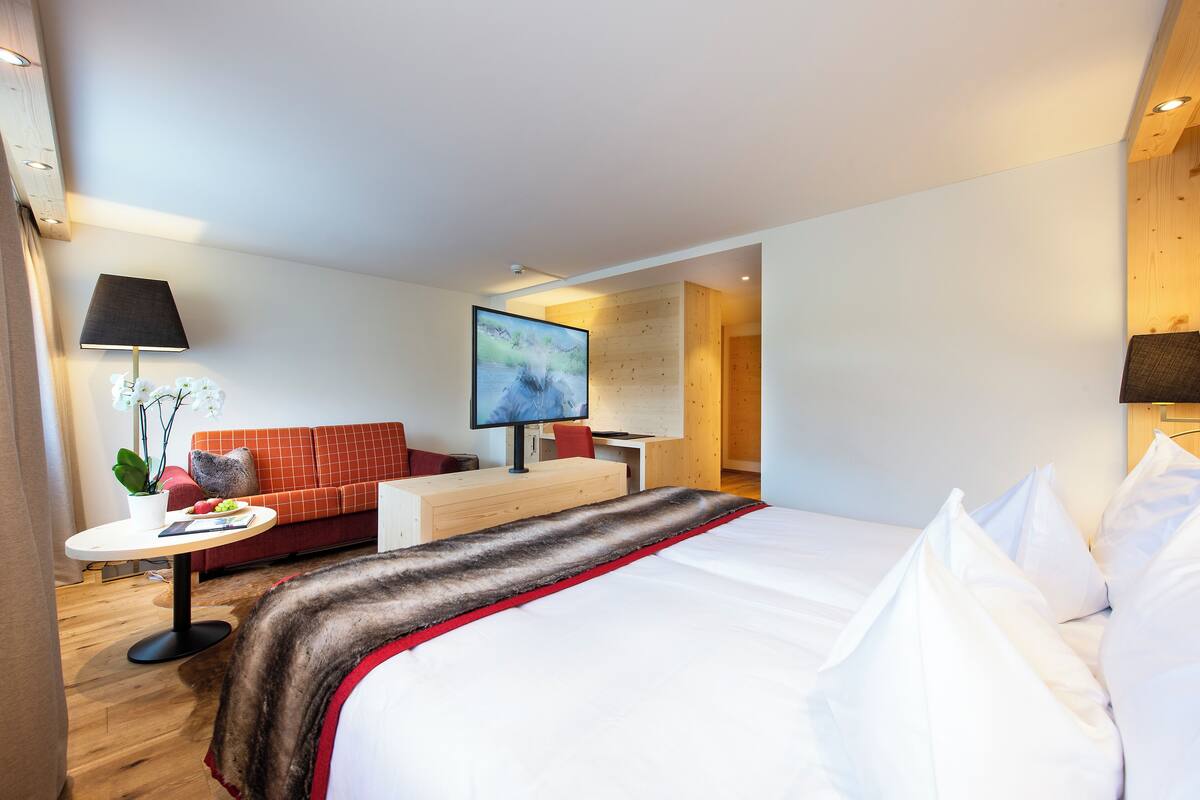 A modern hotel room with a large bed, a sofa, a desk, and a TV.