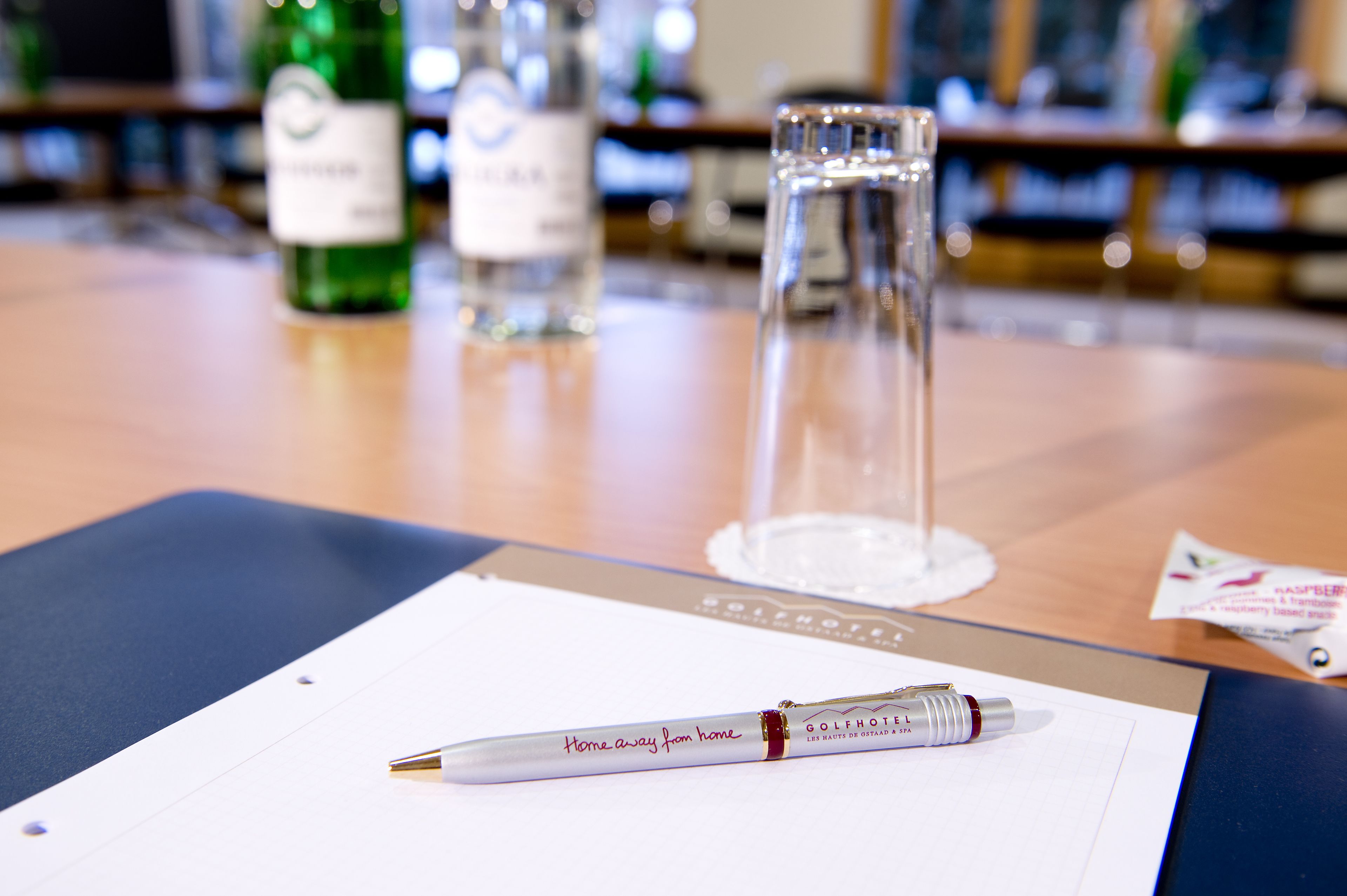 A pen on a clipboard with a label, a glass, and bottles in the background.