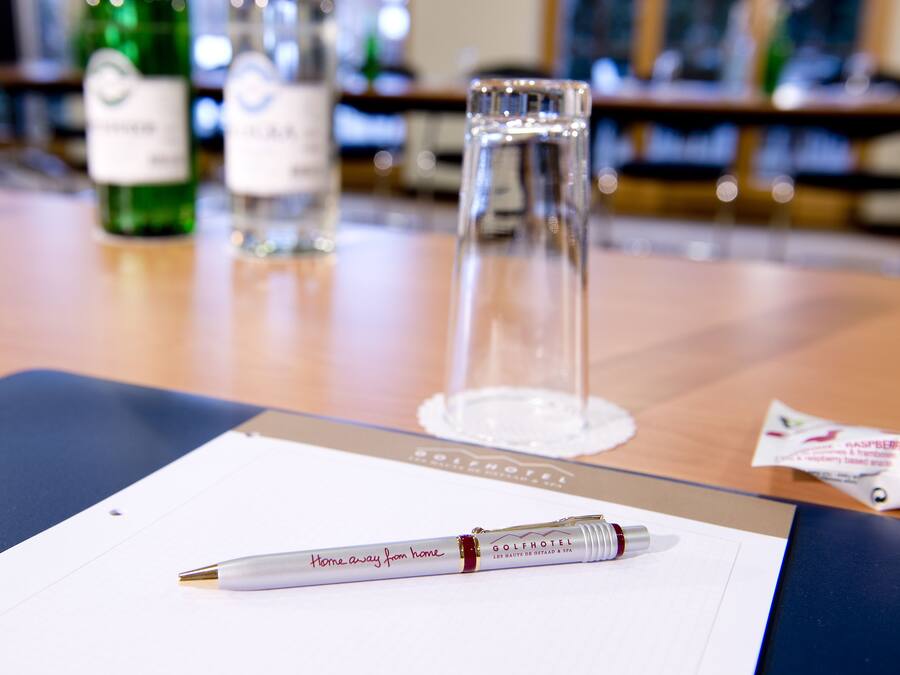 A pen on a clipboard with a label, a glass, and bottles in the background.
