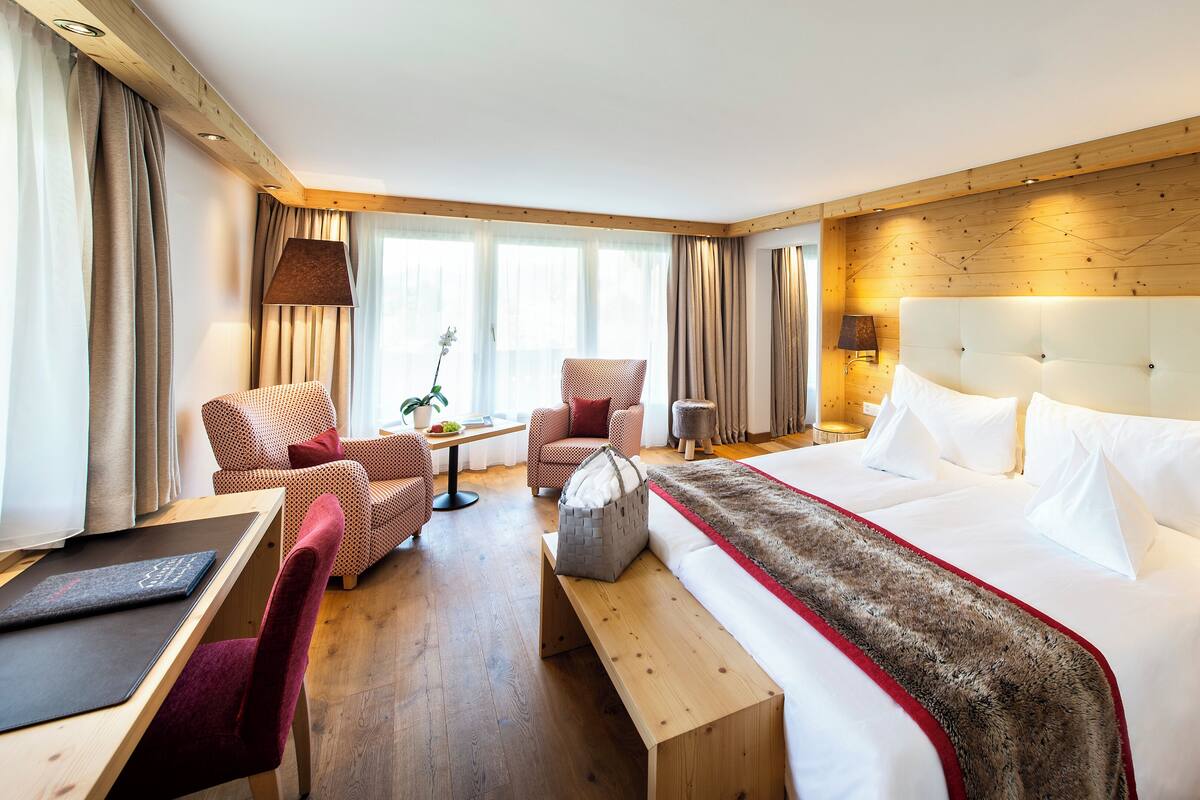 A hotel room with a large bed, two armchairs, a small table, and a desk with a chair.