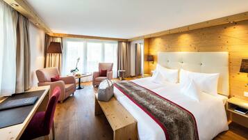 A hotel room with a large bed, two armchairs, a small table, and a desk with a chair.