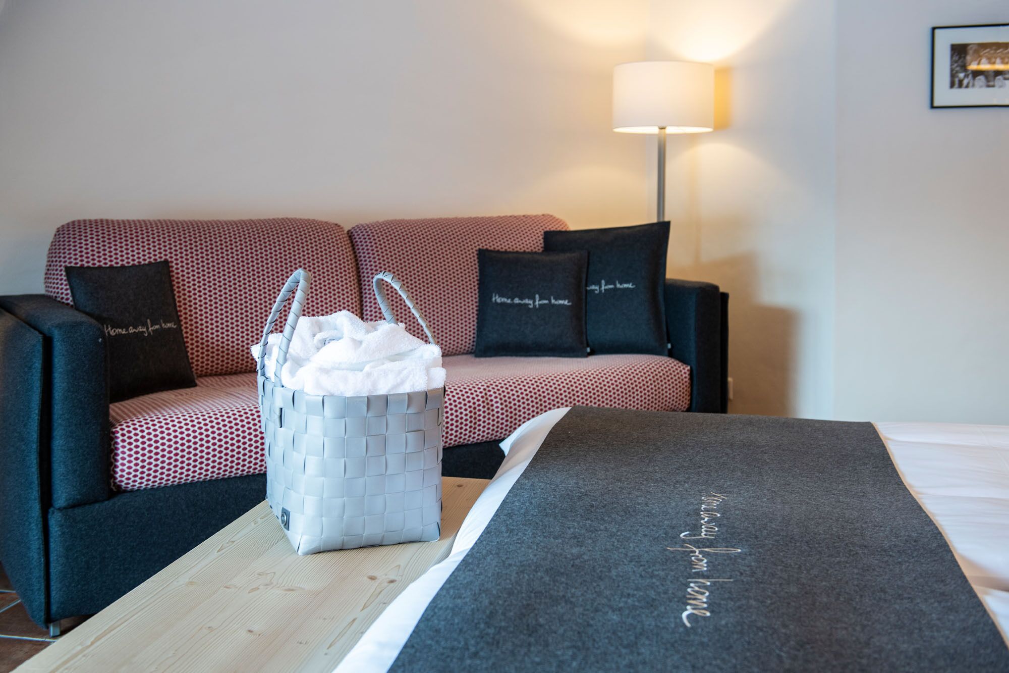 A hotel room with a red and black patterned sofa, a white woven basket, and a black and white throw blanket on a wooden table.