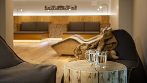 A cozy seating area with a wooden bench and a round wooden table with two glasses of water. - Golfhotel Les Hauts de Gstaad & SPA (Saanen)