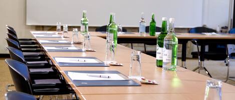 Un salón de conferencias con una larga mesa, sillas, y varias botellas y vasos.