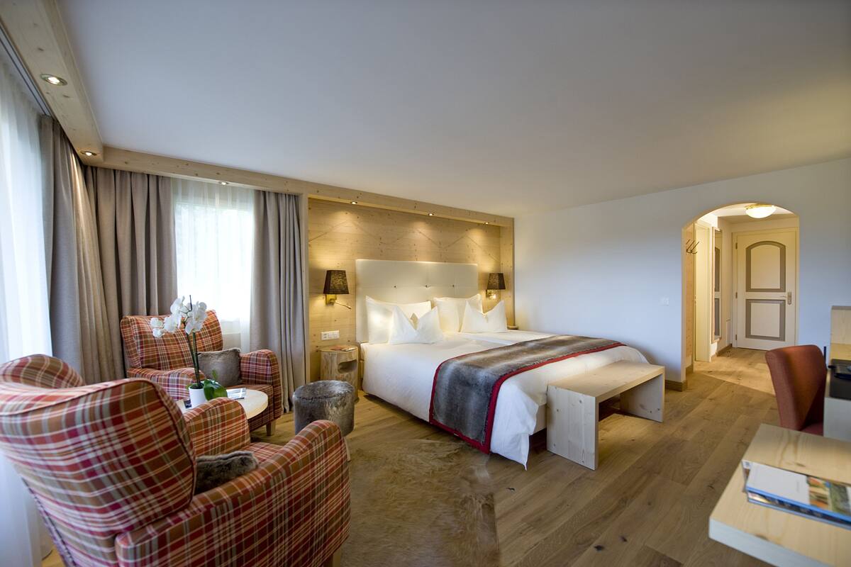 A hotel room with a bed, two armchairs, a small table, and a wooden floor.