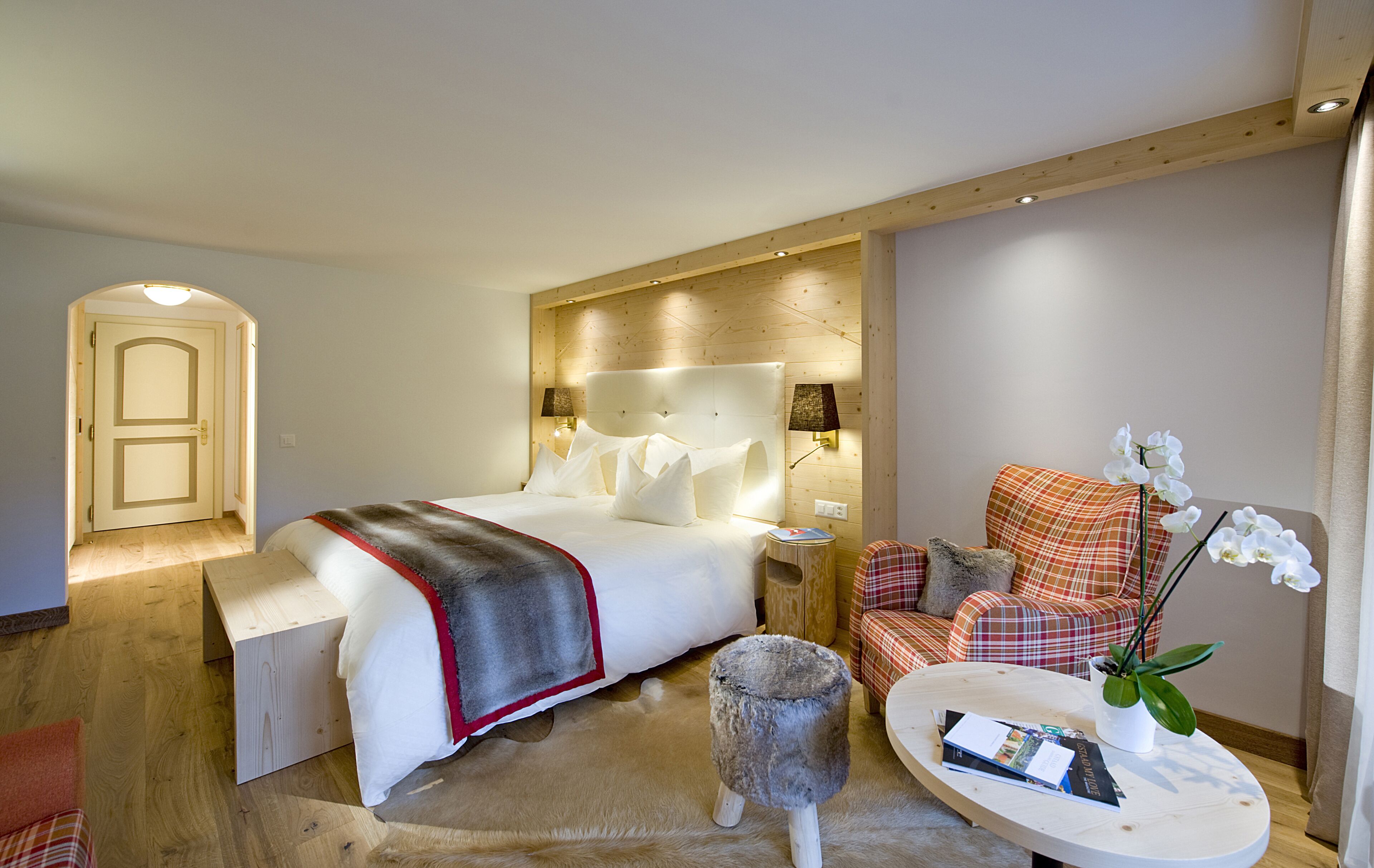 Ein Hotelzimmer mit Bett, Nachttisch, Sessel, kleinem Tisch und einer Zimmerpflanze.