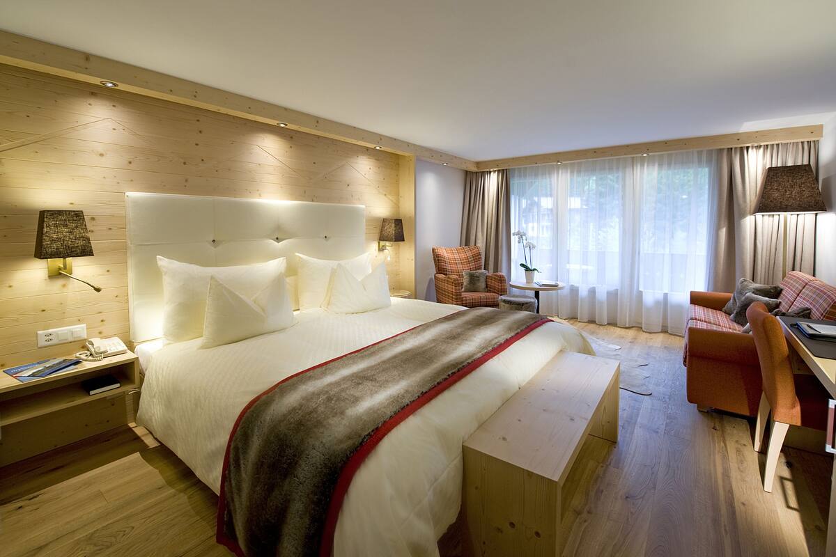A modern hotel room with a large bed, a desk, a chair, and a sofa.