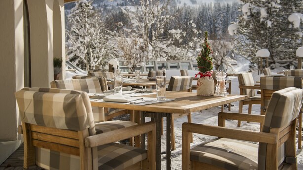 A restaurant with wooden tables and chairs, a Christmas tree, and a snowy mountain view. - Golfhotel Les Hauts de Gstaad & SPA (Saanen)