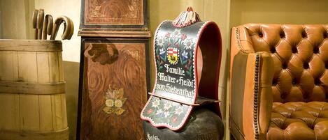 A traditional wooden barrel, a decorative wooden cabinet, and a leather armchair in a room with stone flooring.