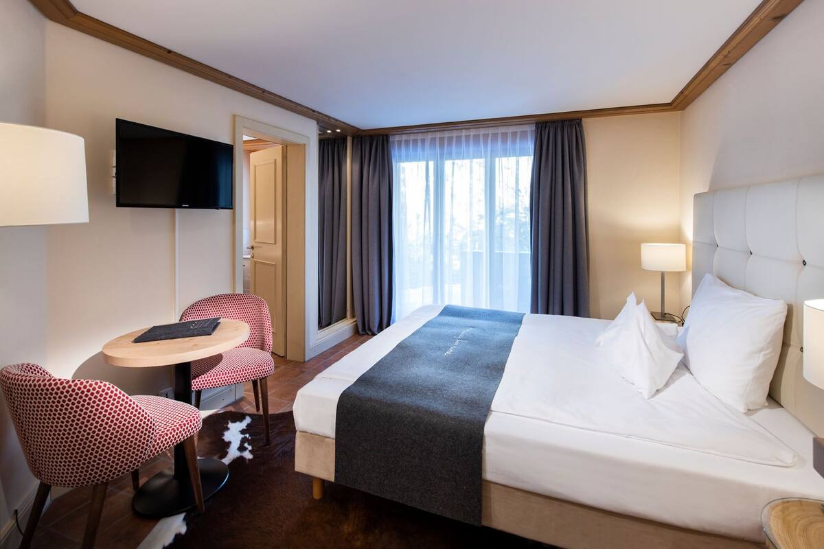 A hotel room with a bed, a desk, a chair, a TV, and a window with curtains.