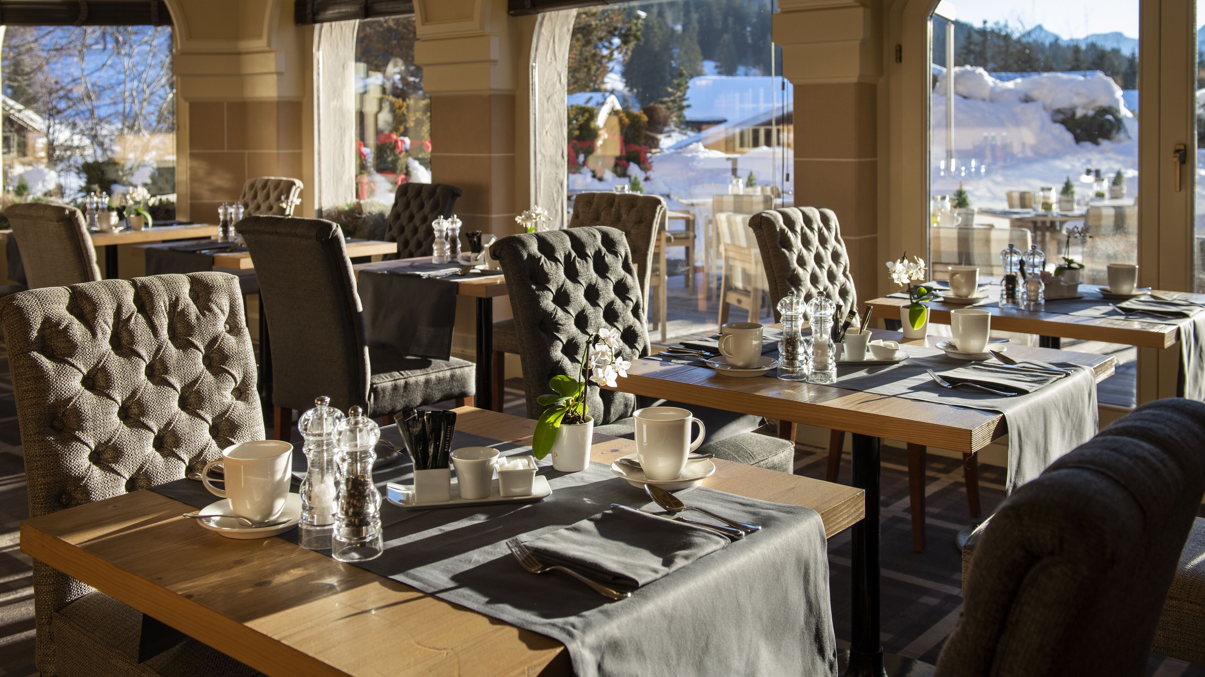 En restaurant med dækkede borde, polstrede stole og udsigt til sneklædte bjerge.