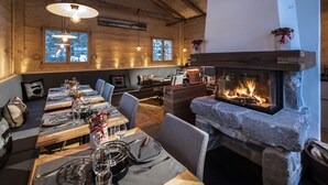 A cozy restaurant with wooden walls, a stone fireplace, and a dining area with tables set for two. - Golfhotel Les Hauts de Gstaad & SPA (Saanen)