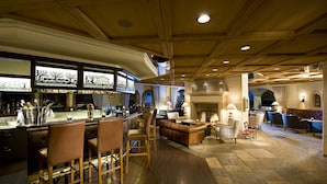 A bar area with stools, a fireplace, and a seating area with couches and chairs. - Golfhotel Les Hauts de Gstaad & SPA (Saanen)