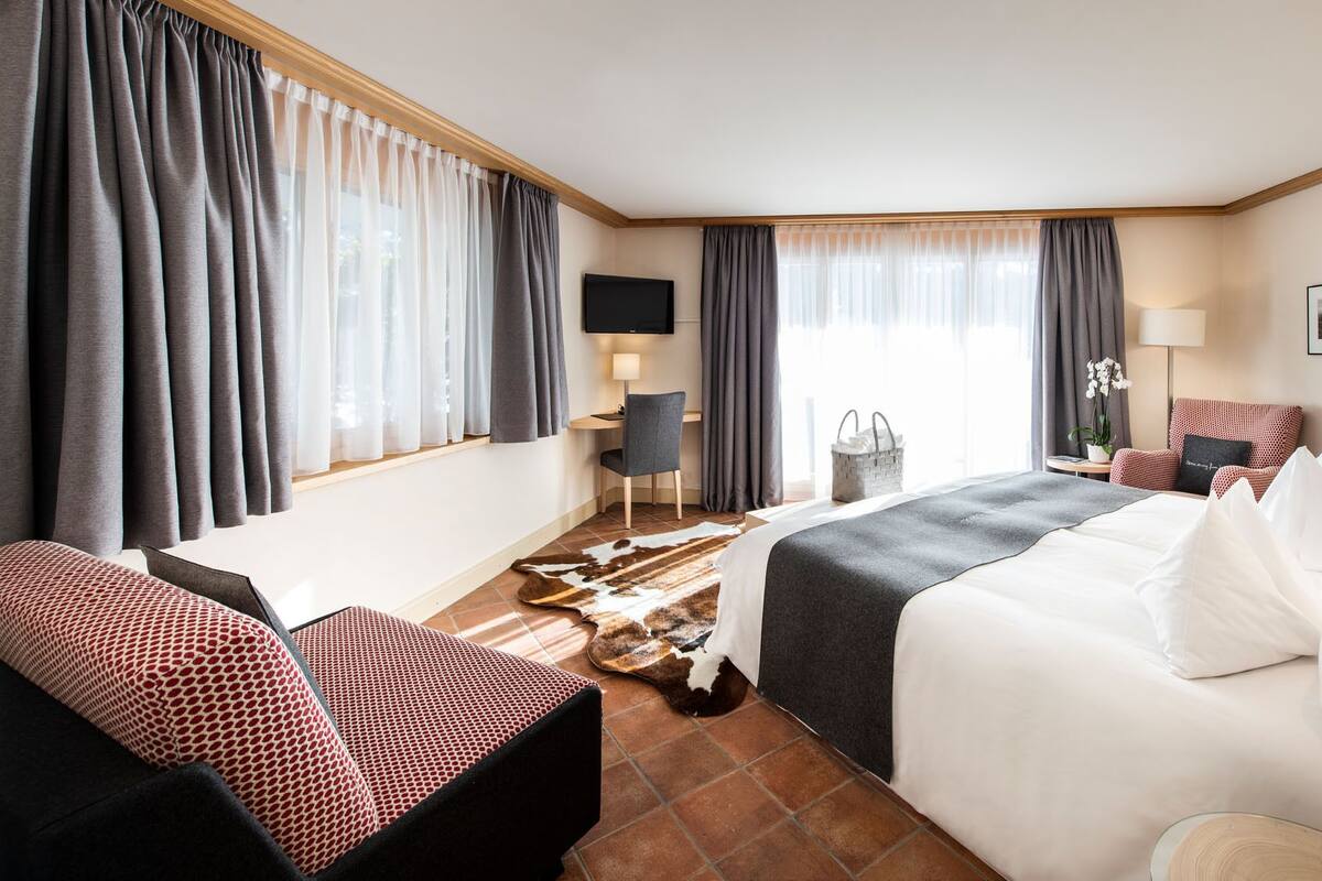 A hotel room with a bed, a desk, a chair, a TV, and a window with curtains.