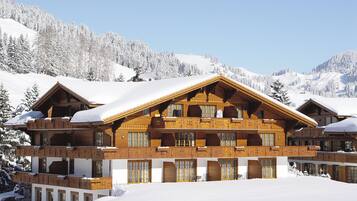 A large wooden chalet with multiple balconies, surrounded by snow-covered mountains.