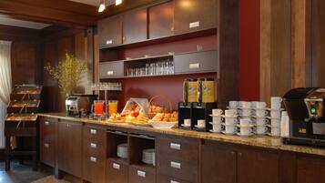 A breakfast bar with a coffee machine, a fruit basket, and a variety of breakfast items.