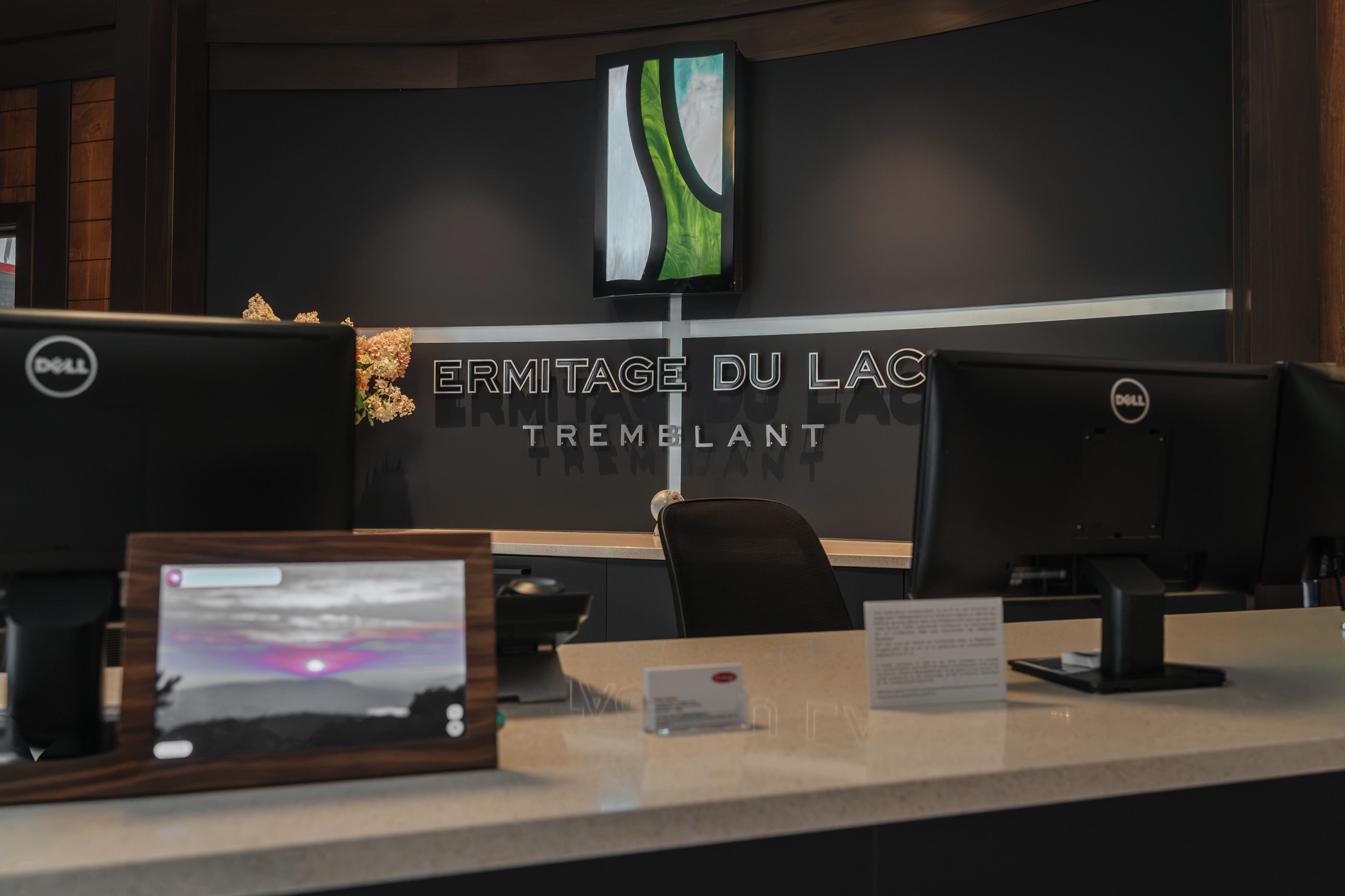 Ein moderner Büroraum mit einem großen Bildschirm, der eine Landschaft zeigt, einem Schild mit der Aufschrift 'ERMITAGE DU LAC TREMBLANT' und mehreren Arbeitsplätzen mit Dell-Computern.