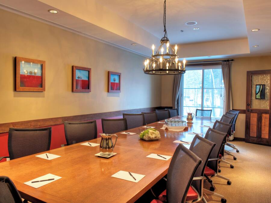 A conference room with a long table, chairs, a chandelier, and framed artwork on the walls.