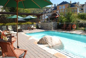A pool area with lounge chairs and umbrellas, surrounded by stone walls and a wooden deck.