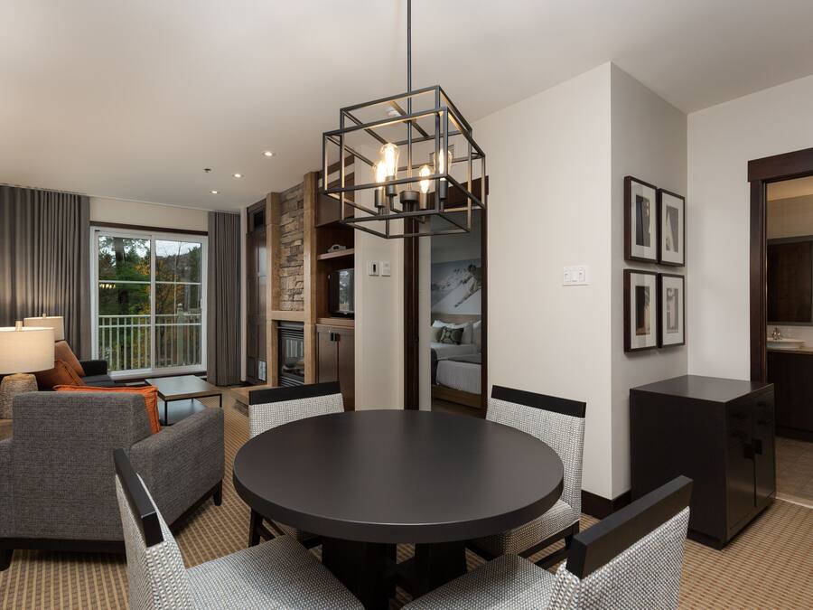 Et moderne hotelværelse med spiseplads, sofa, lampe, tekøkken og et stort vindue.
