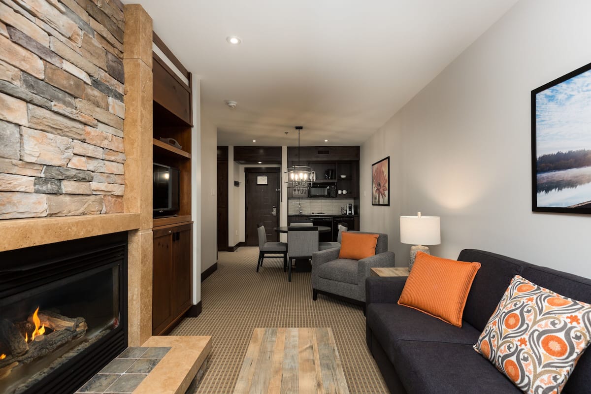 A modern living room with a fireplace, a sofa, a coffee table, and a dining area with a kitchen in the background.