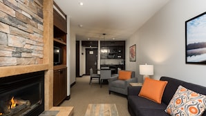 A modern living room with a fireplace, a sofa, a coffee table, and a dining area with a kitchen in the background.