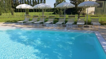 Una piscina con acqua cristallina, circondata da lettini e ombrelloni bianchi.
