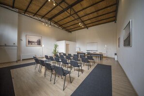 Een vergaderruimte met een hoog plafond, houten balken en een zwart tapijt.