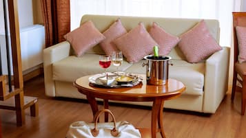 A living room with a sofa, a coffee table with a bottle and glasses, a handbag, and a radiator.