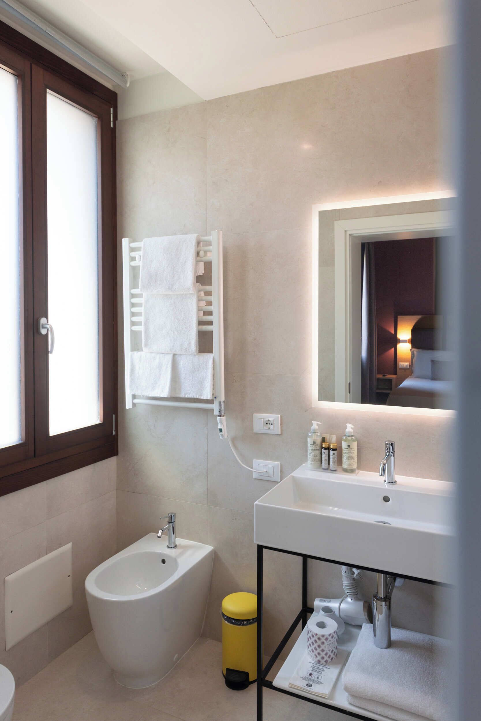 A modern bathroom with a bidet, a sink with toiletries, a towel rack, and a mirror.