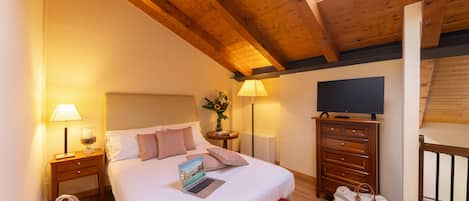 Un dormitorio con una cama, un escritorio con una computadora portátil, un televisor, un aparador y una ventana con vistas.