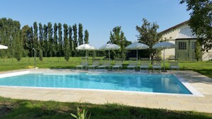 Ein Schwimmbecken mit Liegestühlen und Sonnenschirmen, umgeben von einer Rasenfläche und Bäumen.