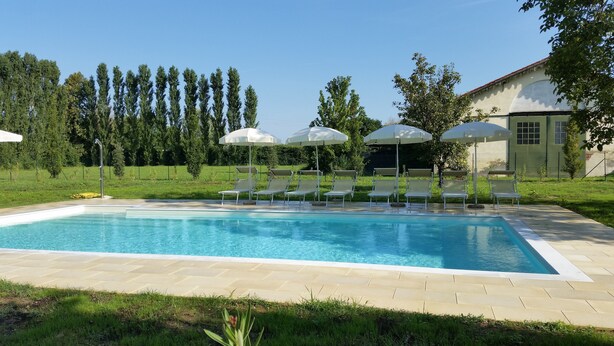 A swimming pool with lounge chairs and umbrellas, surrounded by a grassy area and trees. - Hotel Venice Resort Airport (Mestre)