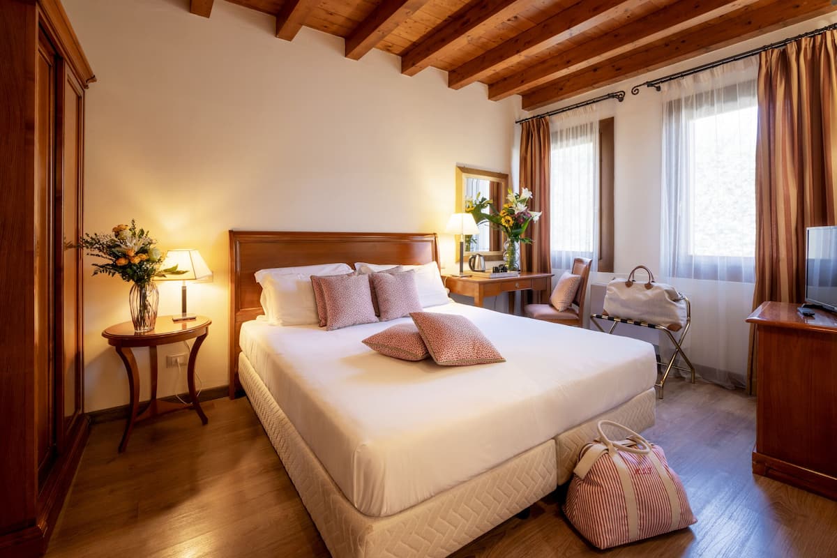 Ein Hotelzimmer mit einem großen Bett, einem Holzkopfstück, Nachttischen mit Lampen, einem Sessel, einem Schreibtisch und einem Fernseher.