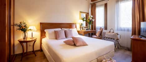 Habitación de hotel con una cama grande, cabecera de madera, mesitas de noche con lámparas, una silla, un escritorio y un televisor.