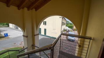 Vista da un balcone con soffitto in legno, zona esterna pavimentata e un'auto parcheggiata sulla strada.