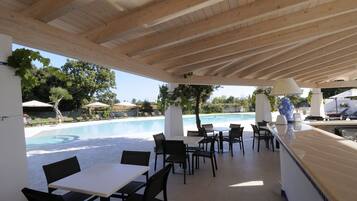 An outdoor pool area with lounge chairs and tables, a wooden ceiling, and a view of the pool.