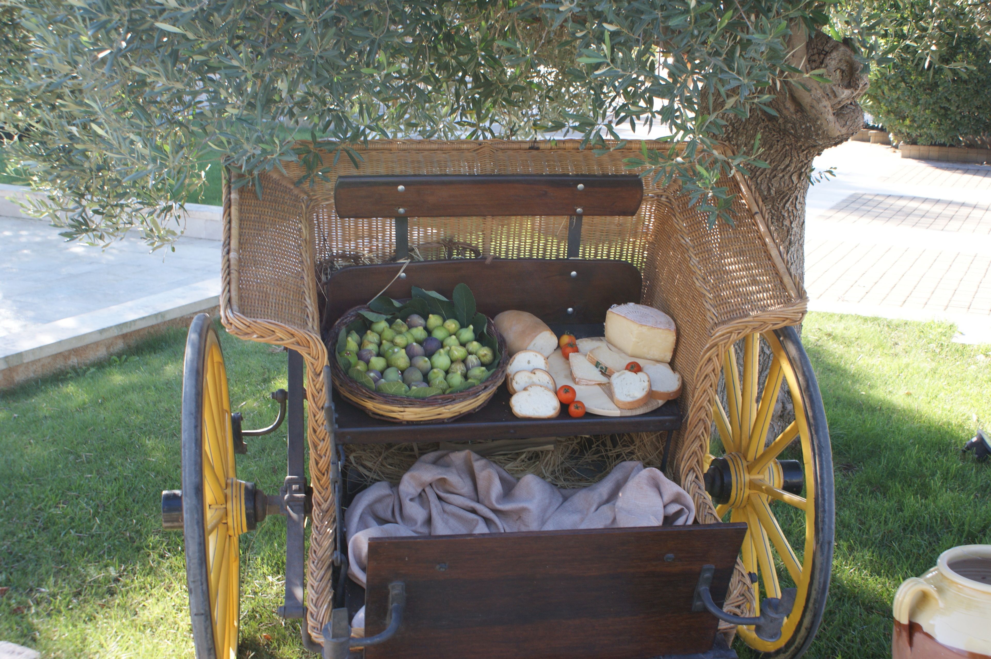 A wicker cart with a basket of green apples, bread, and cheese.