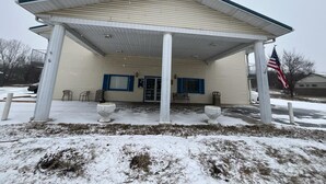 A building with a covered entrance, two windows with blue shutters, and an American flag. - Residential Suites Warrensburg by Hotel O US 50 (Knob Noster)