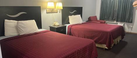 A hotel room with two beds, a nightstand with a lamp, a telephone, and a window with curtains.