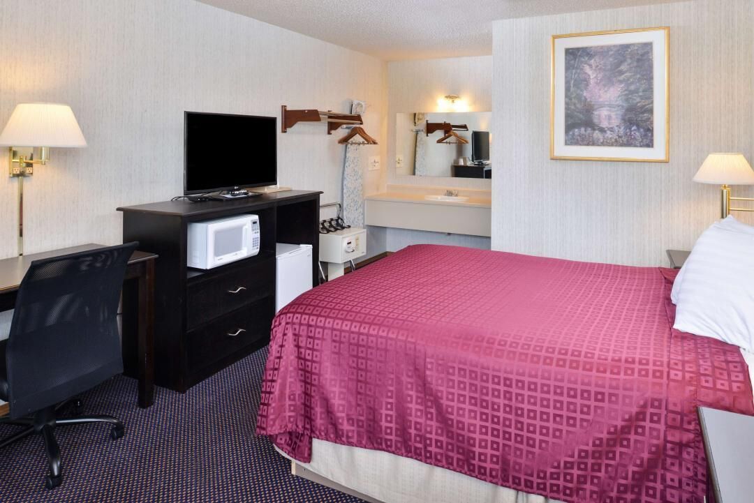 A hotel room with a bed, a desk with a computer, a TV, a mirror, and a painting on the wall.